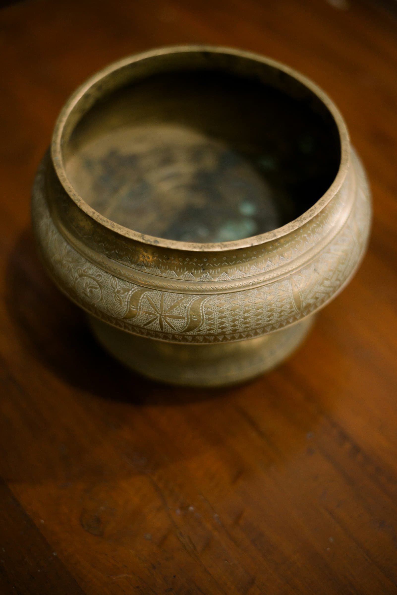 An old engraved brass pot on a dark wooden surface.