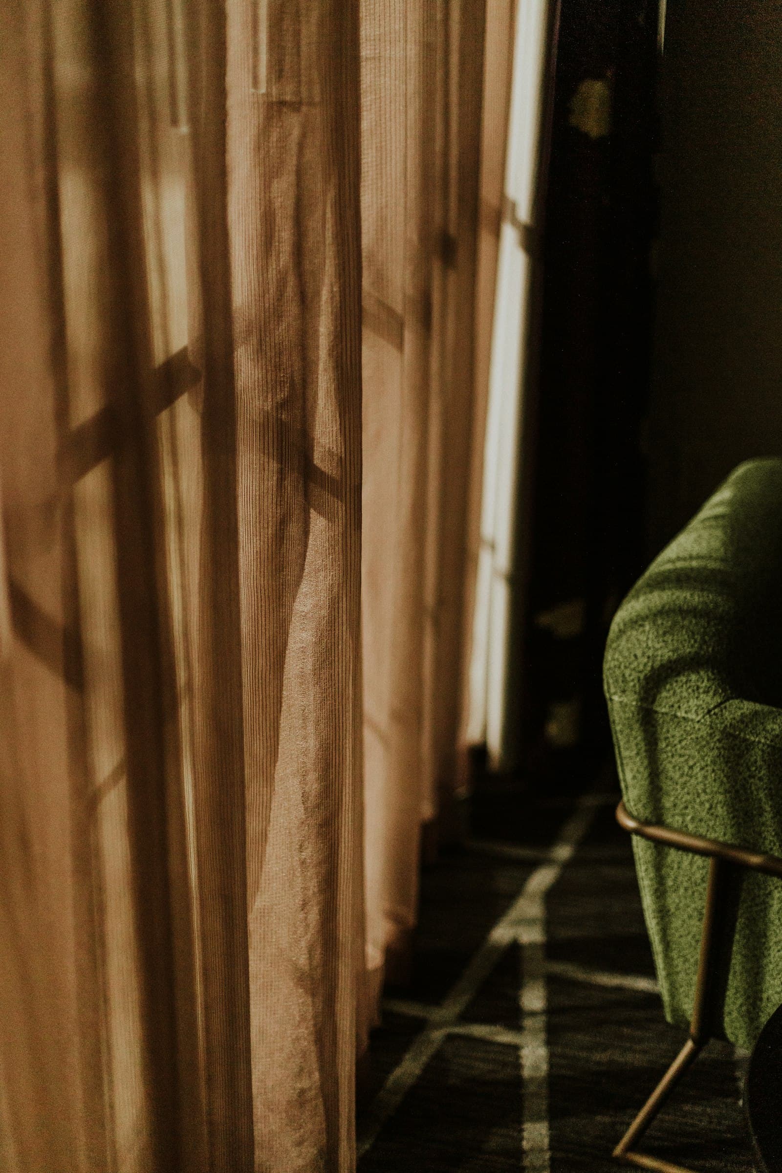 Sunlight through a sheer linen curtain beside a green armchair.