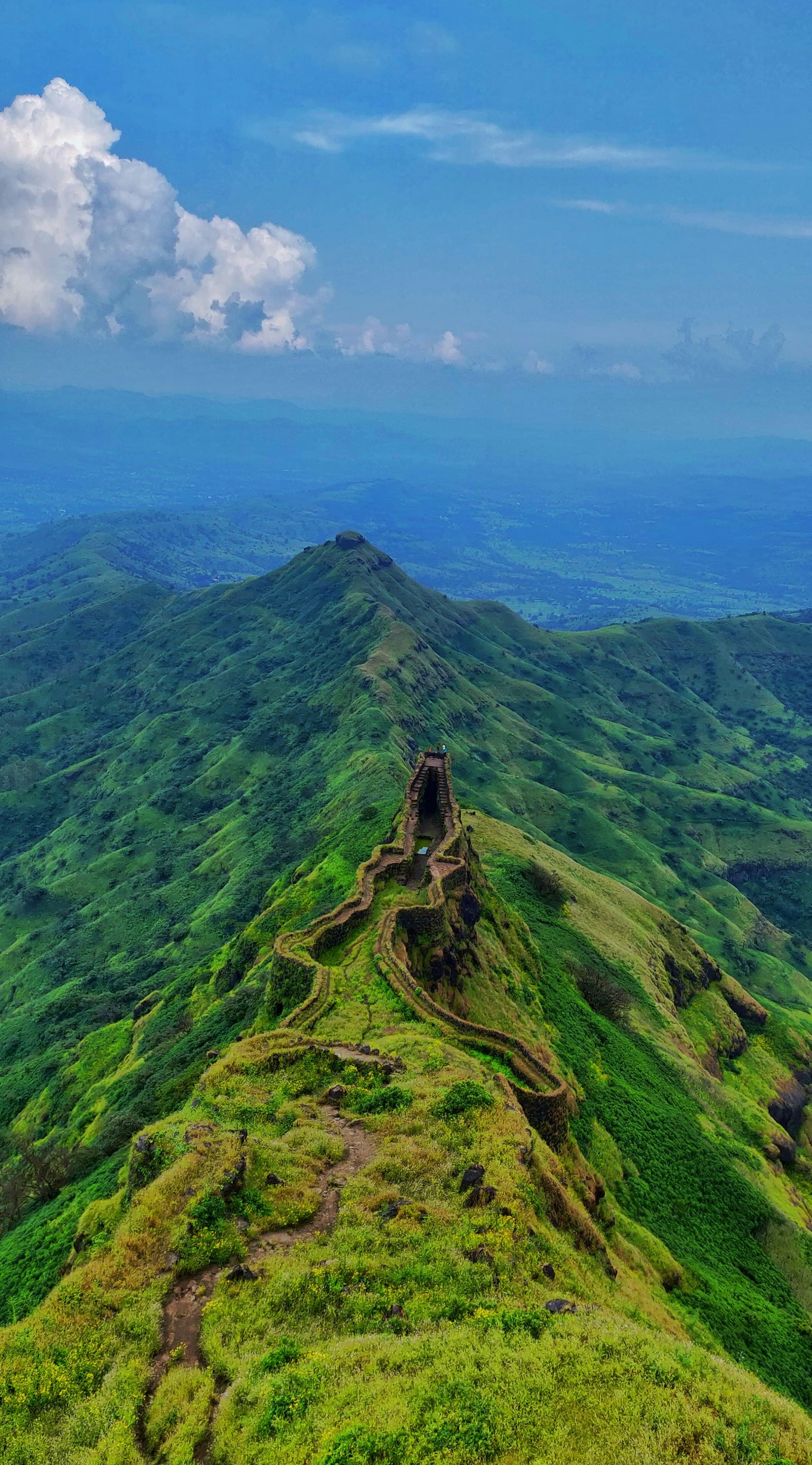 Old stone fort walls running along a green ridge in the hills near Pune.