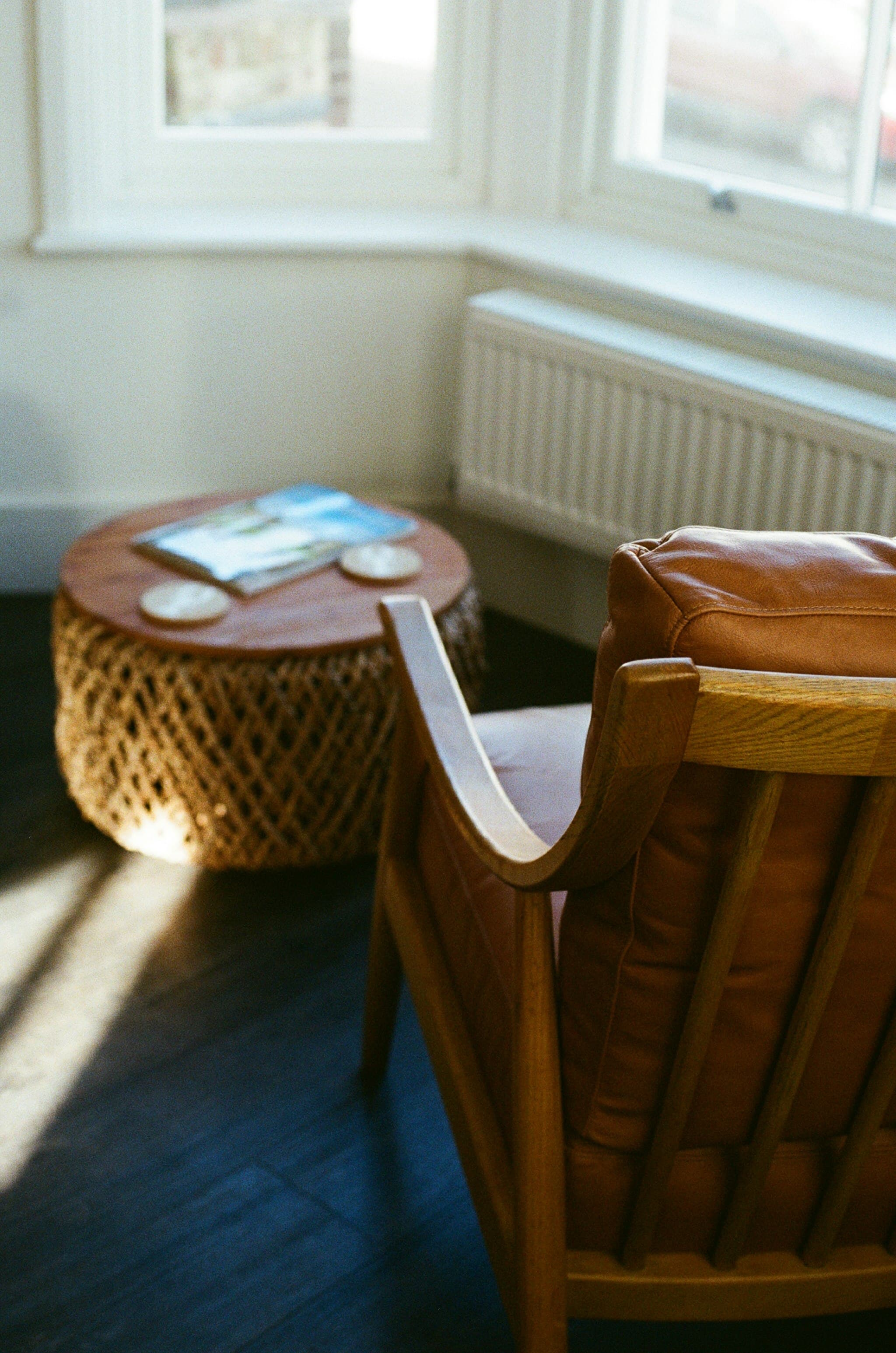 A tan leather armchair beside a woven side table, lit by low sunlight from a window.